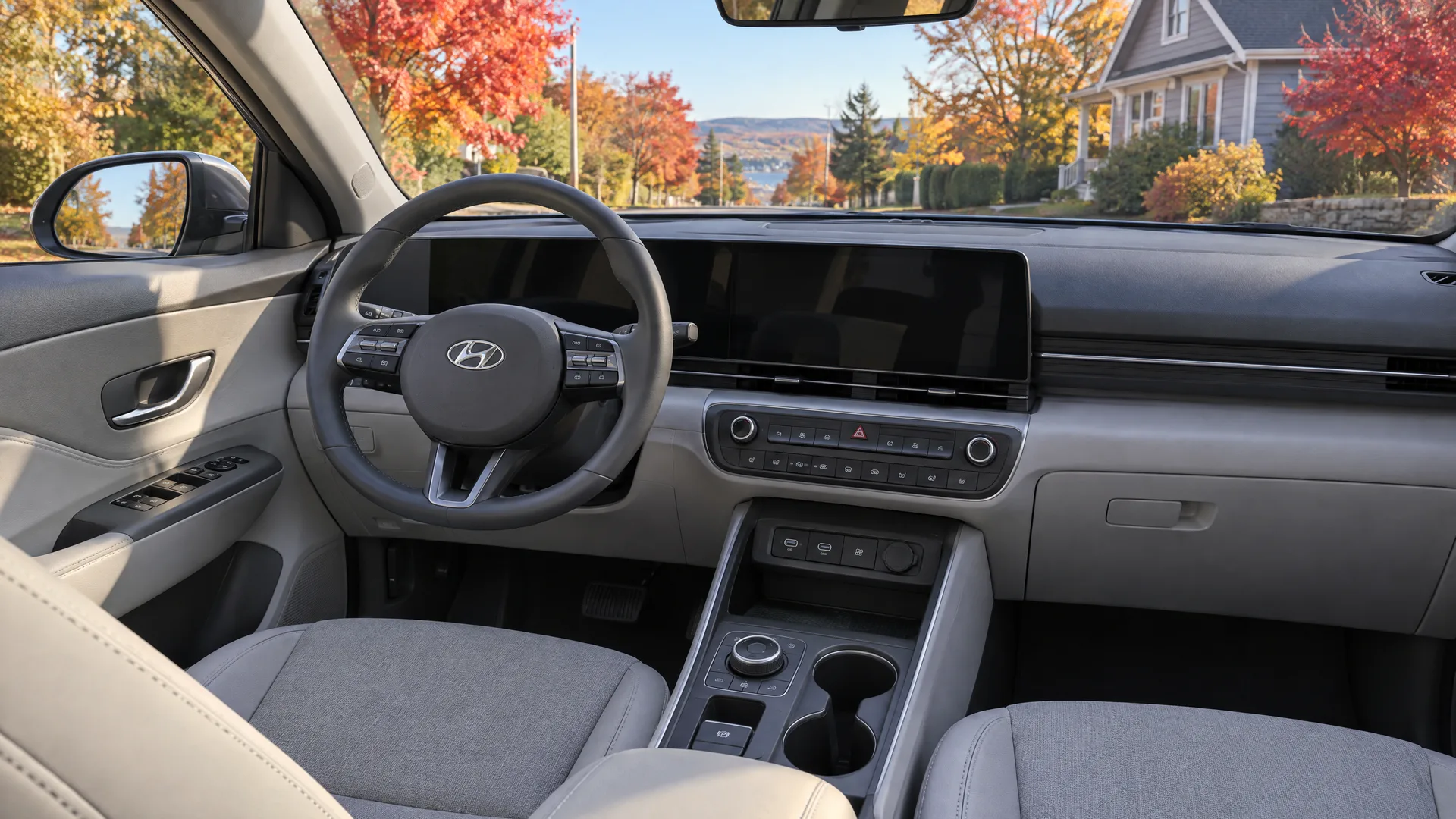 Habitacle d'un Hyundai Kona Electric 2026 vu depuis le siège passager, écran central en veille, sellerie grise, rue d'automne par le pare-brise
