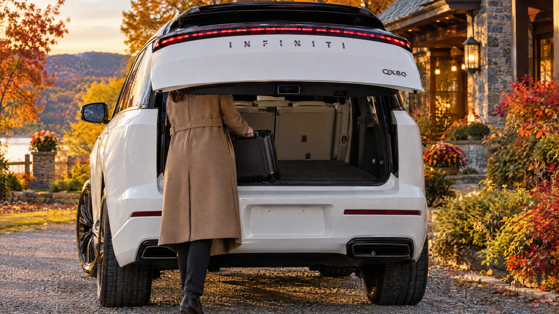Personne de dos qui dépose une valise dans le coffre ouvert d'un INFINITI QX80 2026 blanc, stationnement d'hôtel en Estrie, début de soirée