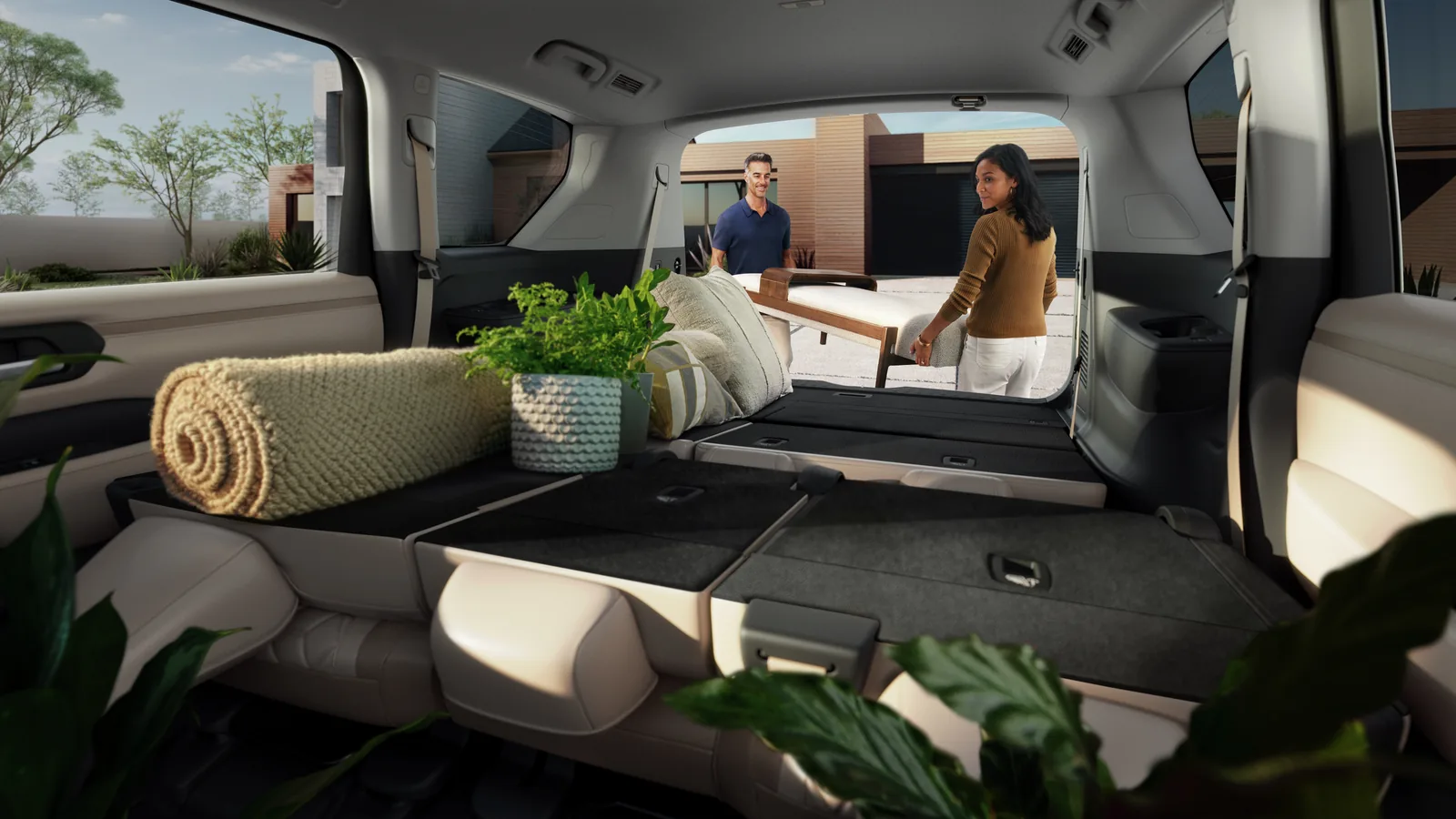 Couple chargeant une table dans un Nissan Armada dont les deuxième et troisième rangées sont rabattues à plat, hayon ouvert devant une maison