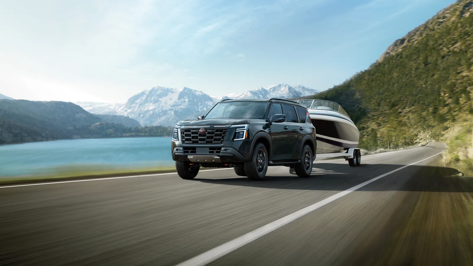 Nissan Armada noir tractant un bateau sur une route de montagne le long d'un lac, sommets enneigés à l'horizon