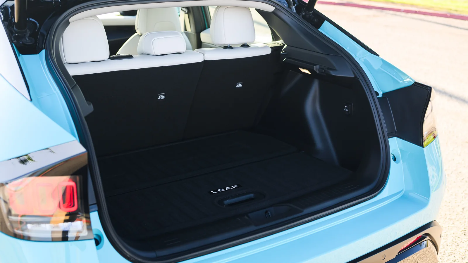 Hayon ouvert d'une Nissan LEAF bleu clair montrant le plancher de coffre plat et la banquette arrière claire