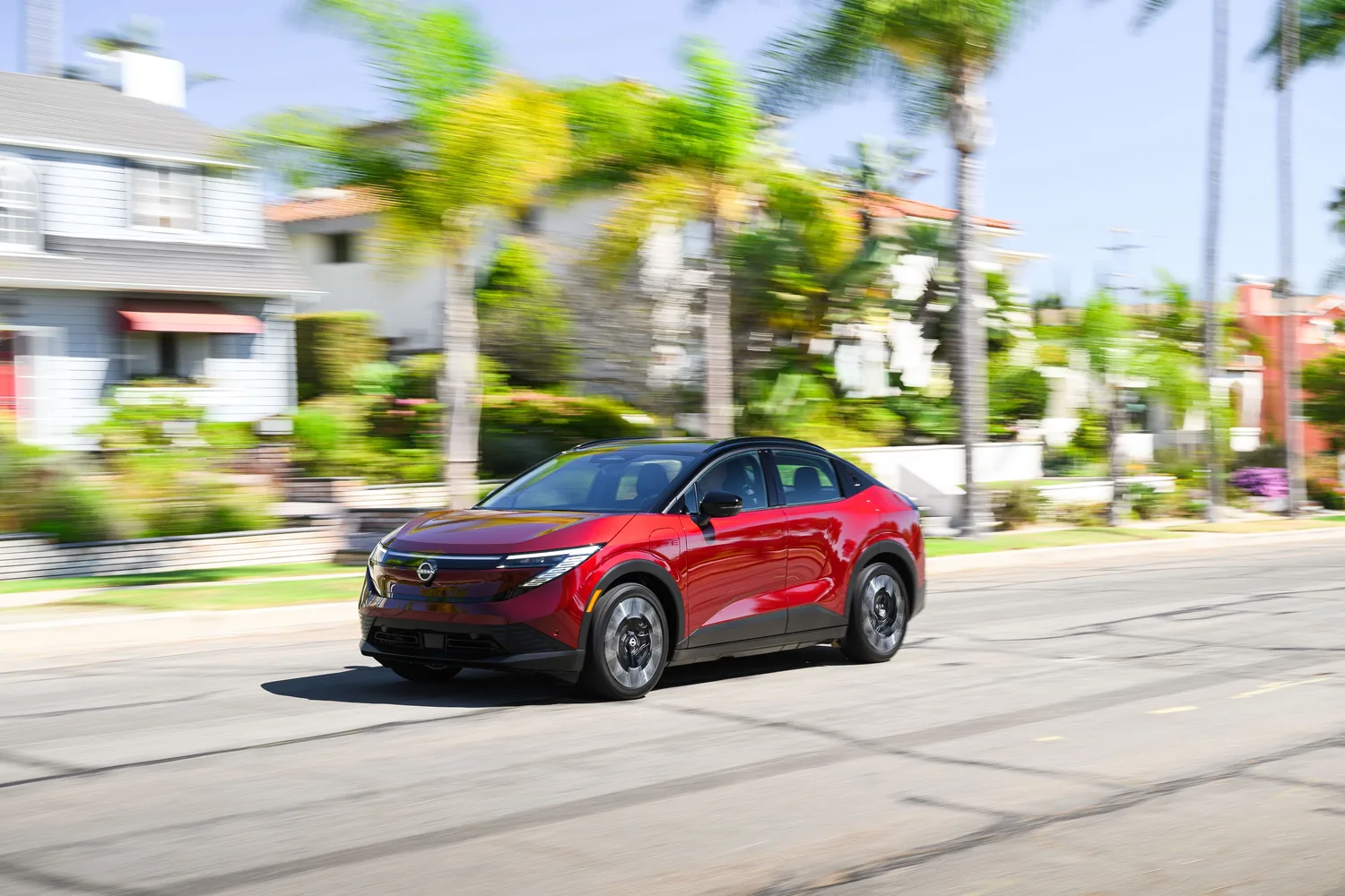 Nissan LEAF rouge de trois quarts avant dans une rue résidentielle bordée de maisons et de palmiers