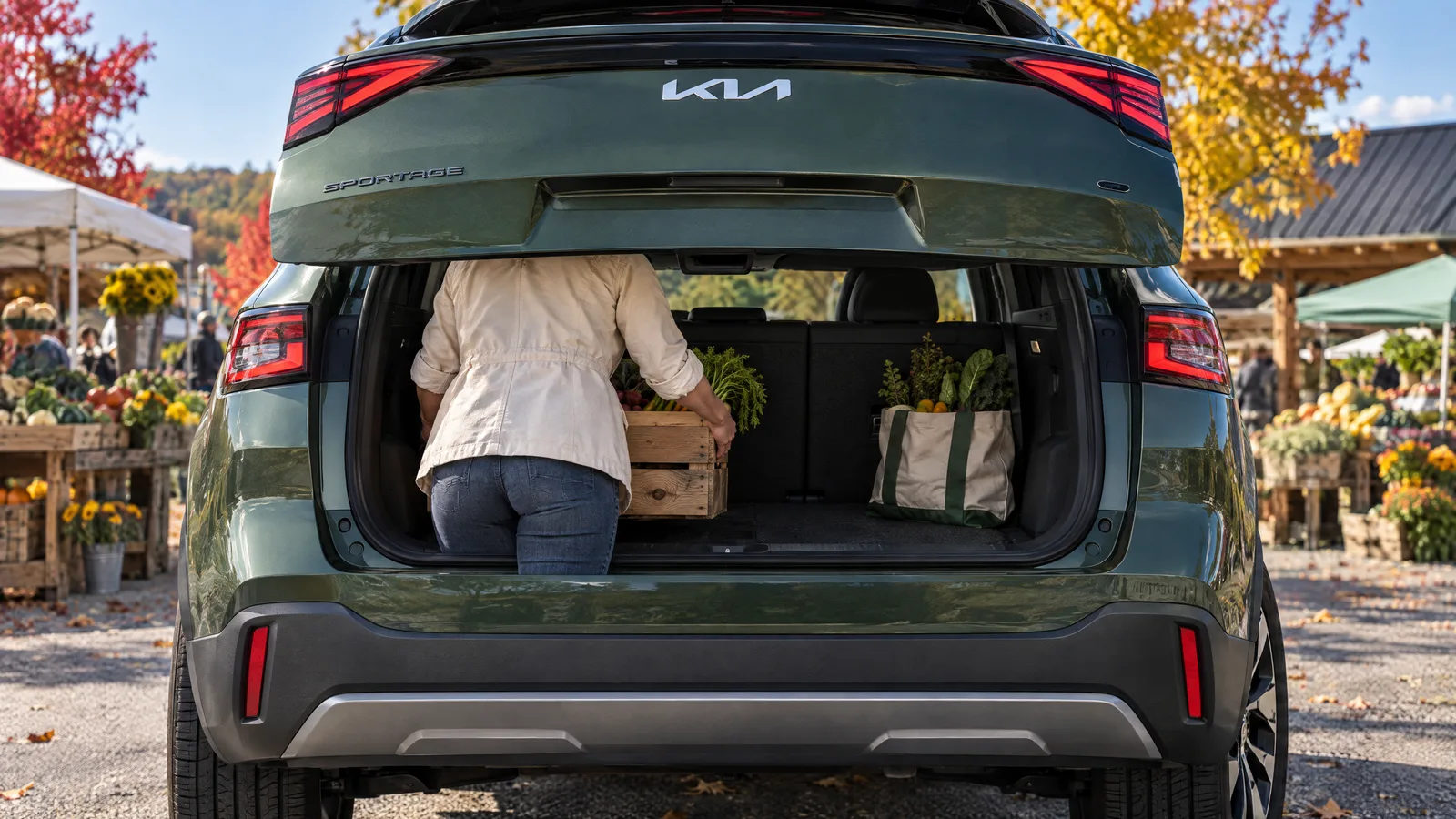Personne de dos qui charge une caisse de bois dans le coffre ouvert d'un Kia Sportage 2026 vert jungle, stationnement d'un marché public en Estrie