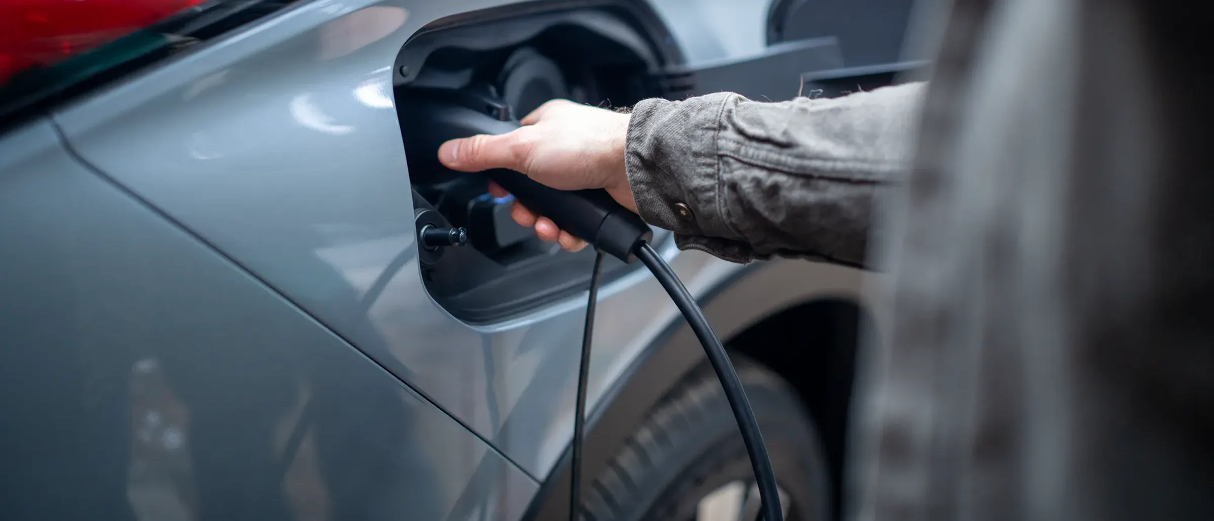 Main qui branche le câble de recharge dans la prise d’un Mitsubishi Outlander PHEV, à la maison.