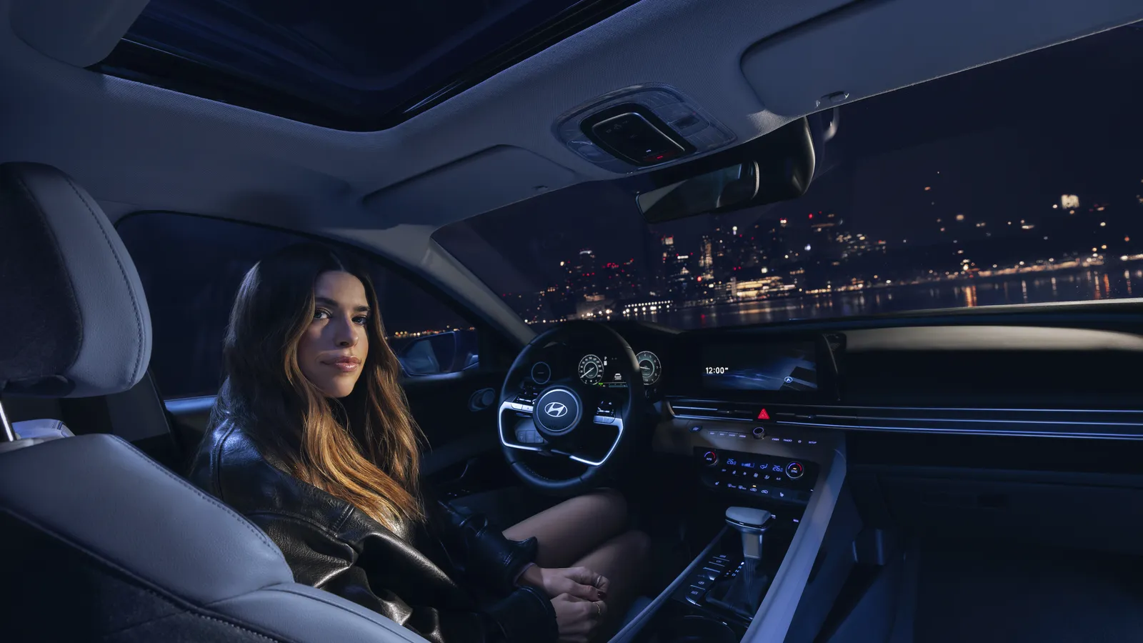 Habitacle d’une Hyundai Elantra 2026 vu depuis la banquette arrière, de nuit, écrans allumés et ville en arrière-plan.