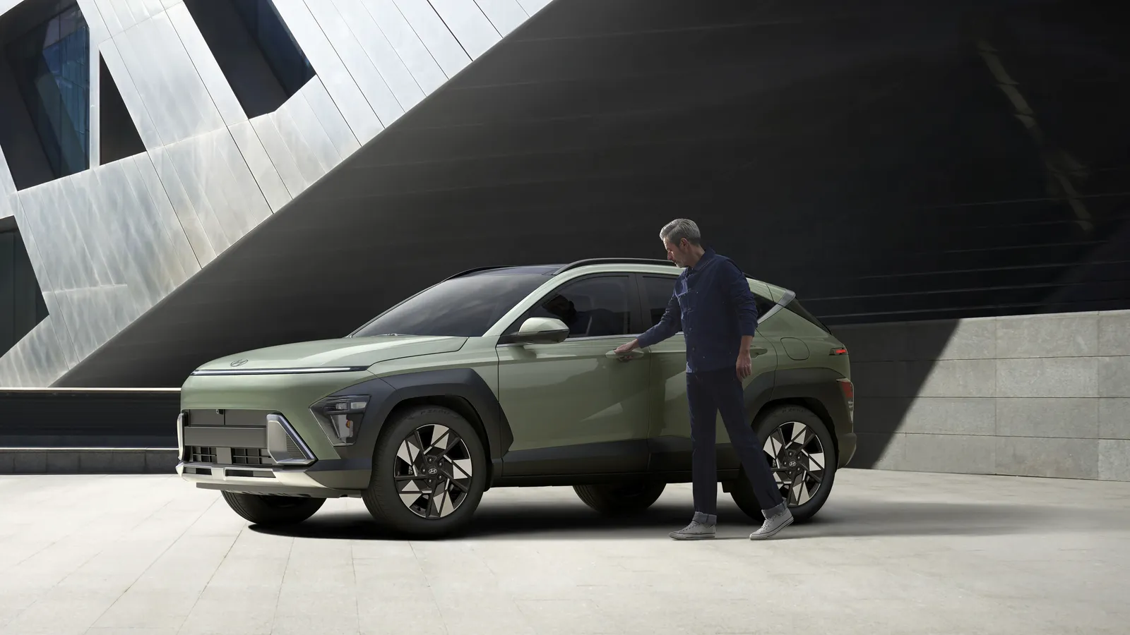 Hyundai Kona 2026 vert olive stationnée devant un bâtiment contemporain, une personne ouvrant la portière conducteur.