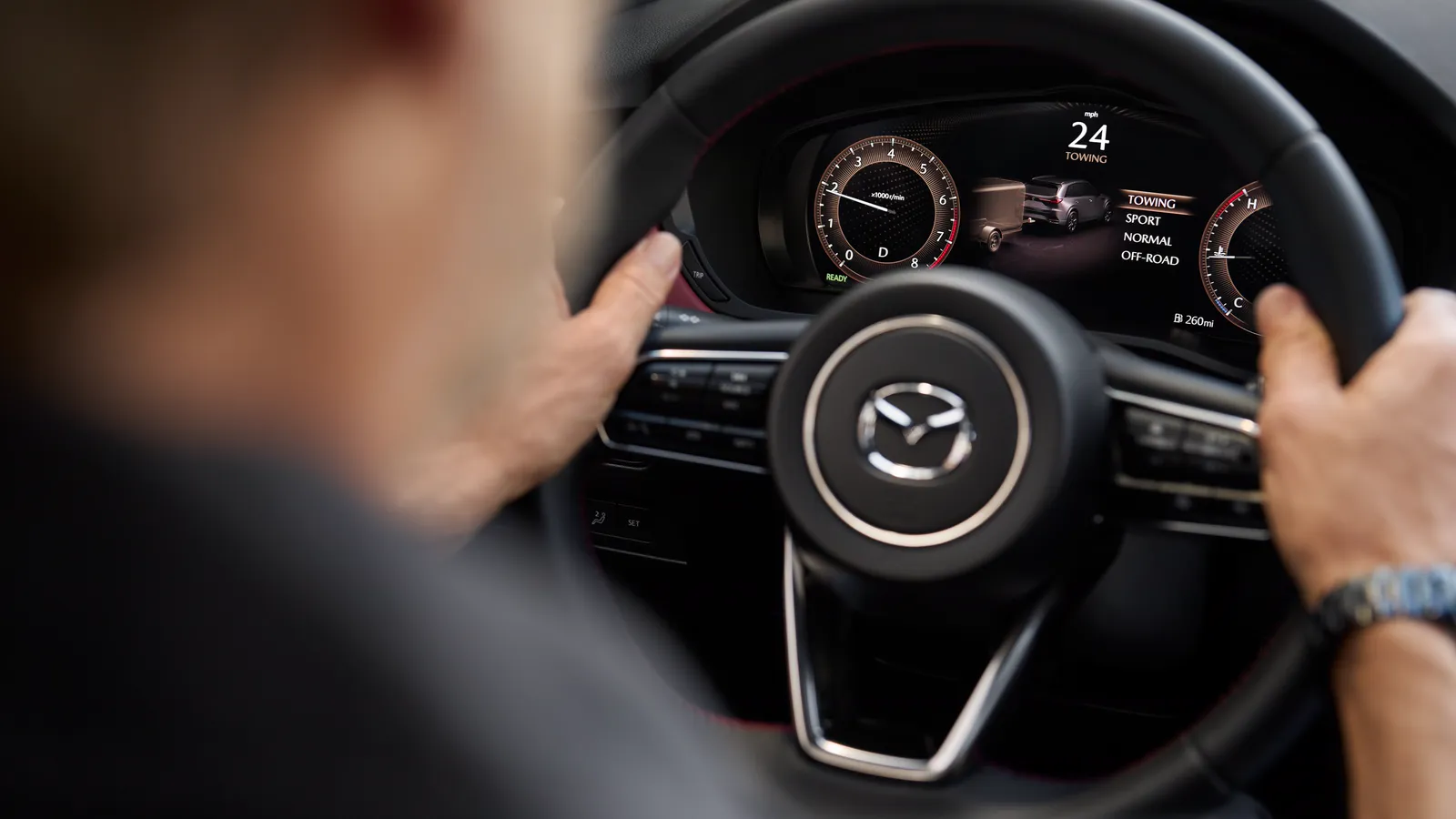Gros plan sur le volant d’un Mazda CX-70 2025, emblème Mazda net au centre, mains du conducteur visibles.