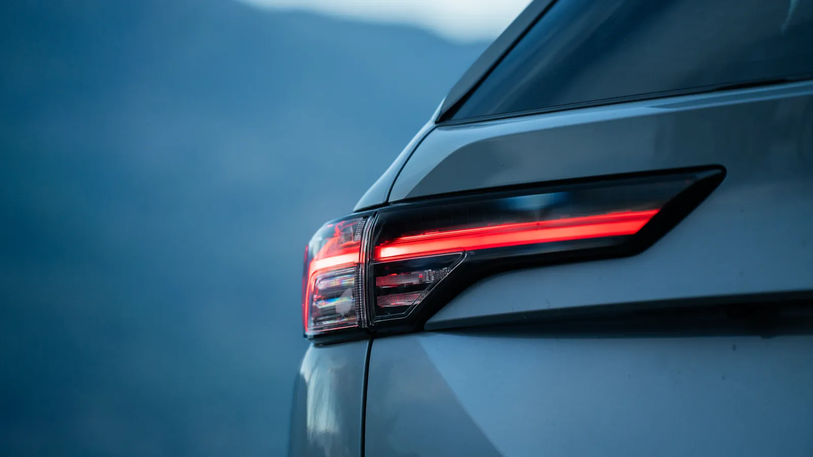 Gros plan sur le feu arrière signature d’un Mitsubishi Outlander PHEV 2026 gris allumé à la tombée du jour, montagnes en arrière-plan.